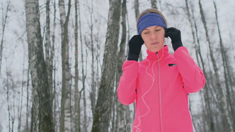 A-young-girl-on-the-morning-jog-holds-in-her-hands-a-smartphone-picks-a-music-track-for-training.-Winter-run.-Use-modern-gadgets-and-training-applications